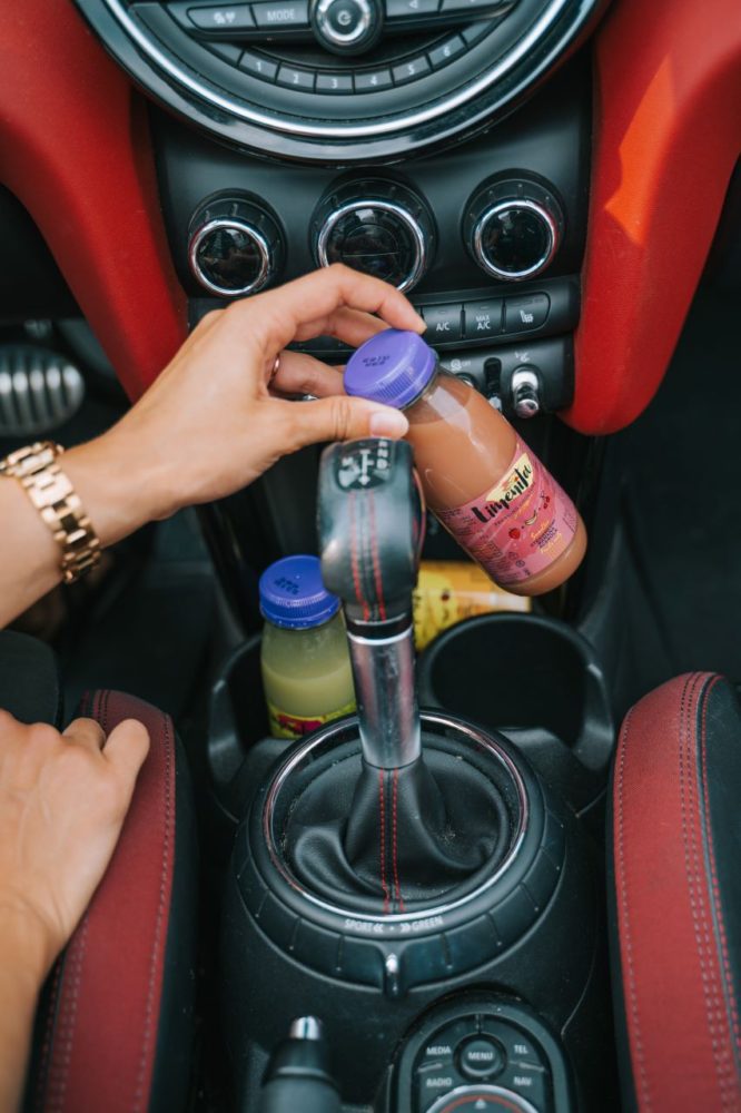 A hand holds a Limeñita bottle in the car, another bottle is in the cup holder next to the gear shift, ready for breakfast.