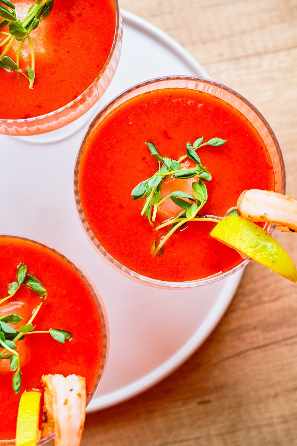 Close-up of vibrant red gazpacho garnished with fresh greens, shrimp, and a lemon slice on the rim.