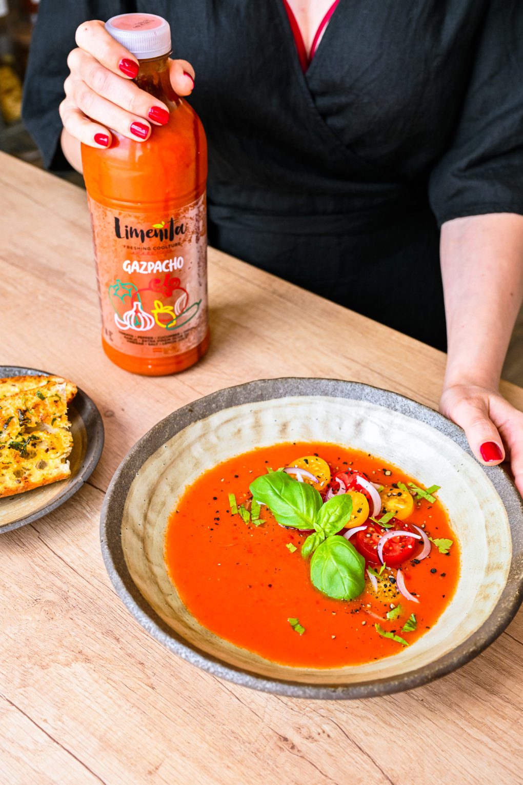 Bright red gazpacho in elegant glasses, topped with fresh herbs, shrimp, and lemon for garnish.